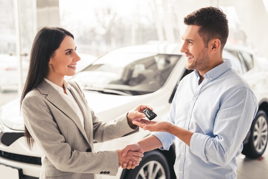 Visiting car dealership. Handsome man is getting car key from beautiful sales manager, shaking her hand and smiling